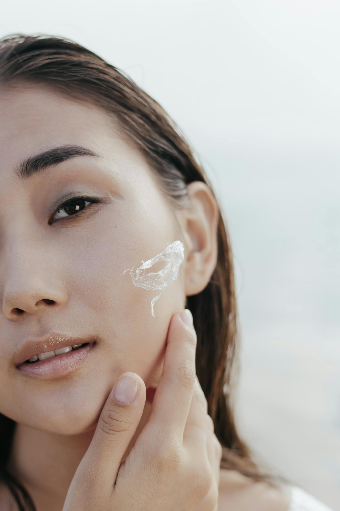 Close-up shot of a woman applying facial cream, promoting skincare and youth.